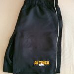Schwarze Sportshorts mit weißen Paspeln und AVTINCA-Stickerei in gelben und weißen Buchstaben am Saum.